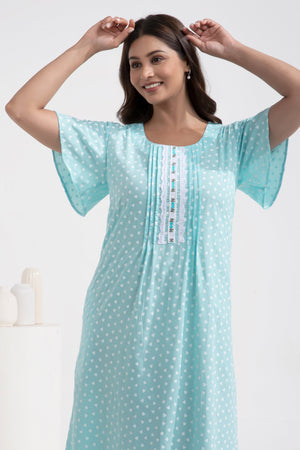 A woman standing in a room wearing a blue nightgown with a polka dot pattern.