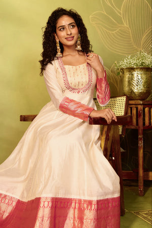 A woman wearing a traditional Festive Indian Anarkali gown in off-white with red and gold zari embroidery.